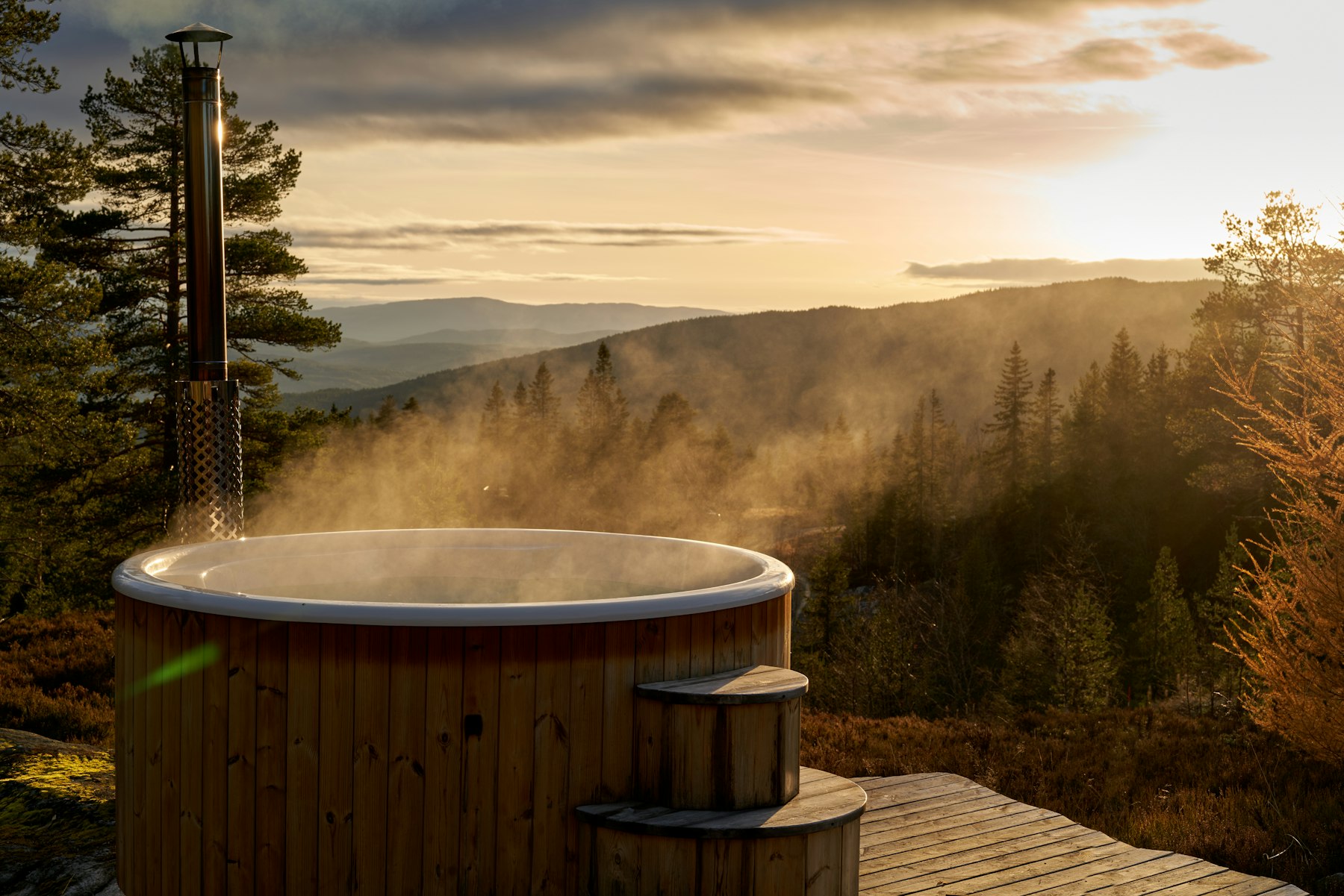 Hot tub on a wooden deck overlooking a forested valley at dusk